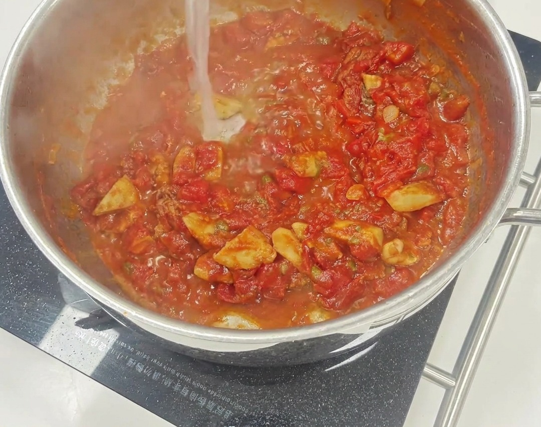 Una vibrante salsa de tomate rojo cociendo a fuego lento en una sartén con trozos visibles de tomates secos y alcaparras.