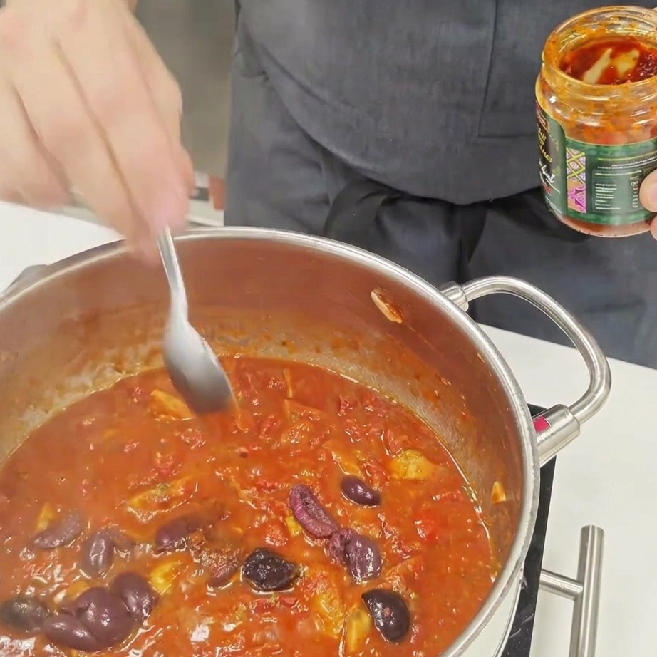 Una cucharada de salsa picante removiéndose en una salsa de tomate burbujeante.