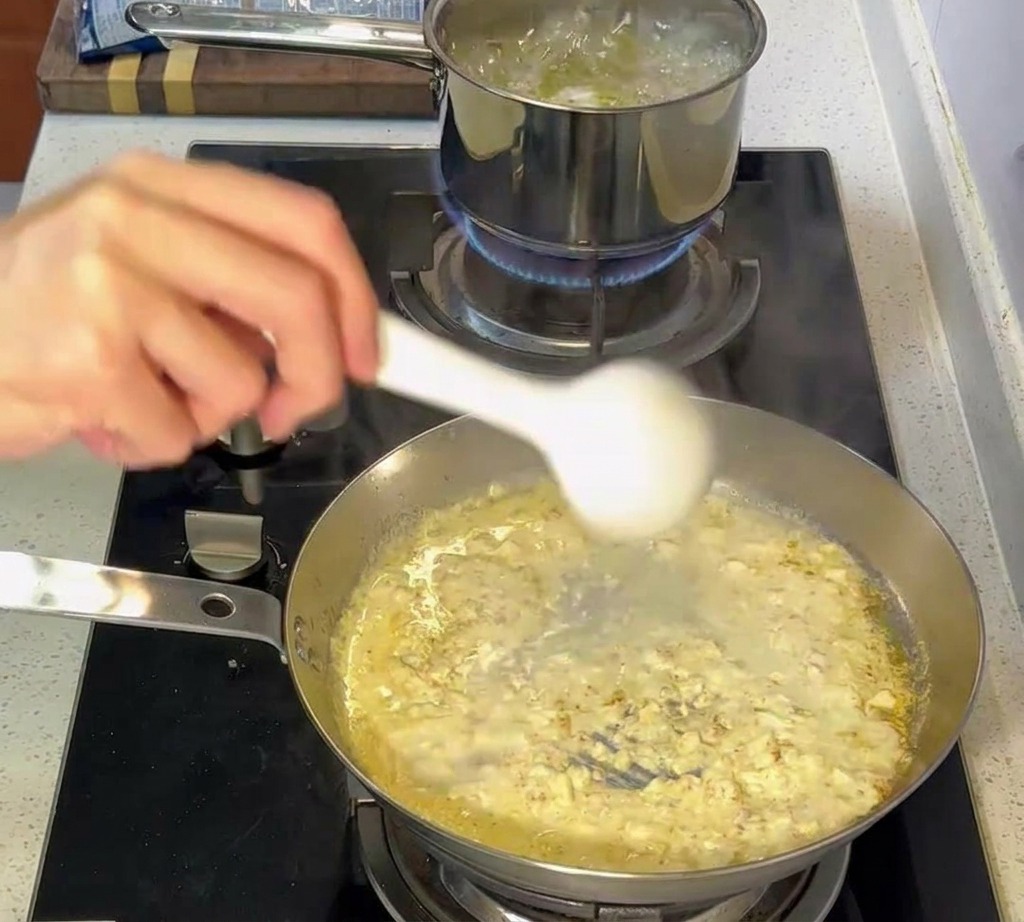 Pinzas transfiriendo pasta al dente de una olla hirviendo a la sartén con salsa cremosa.
