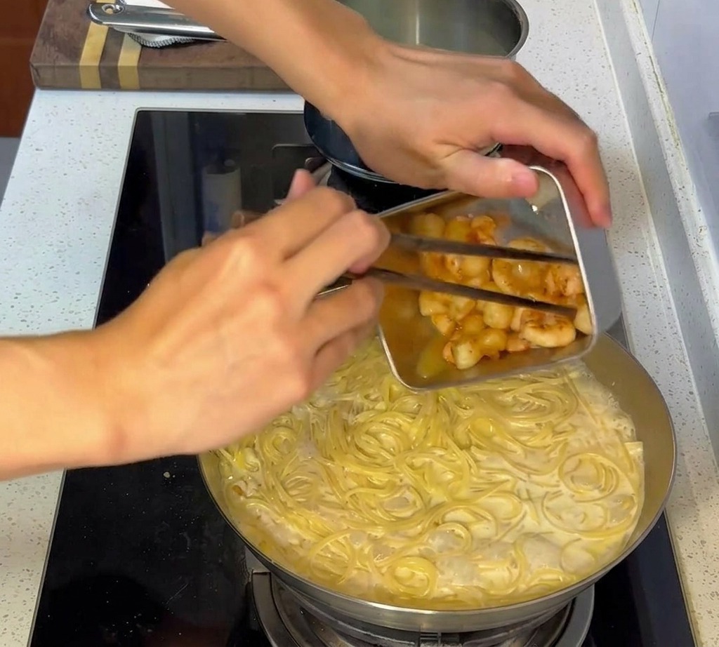 Mariscos salteados siendo añadidos a la sartén con la pasta cremosa mezclada.