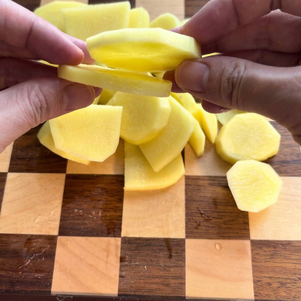 Patatas peladas cortadas cuidadosamente en rodajas sobre una tabla de cortar de madera.