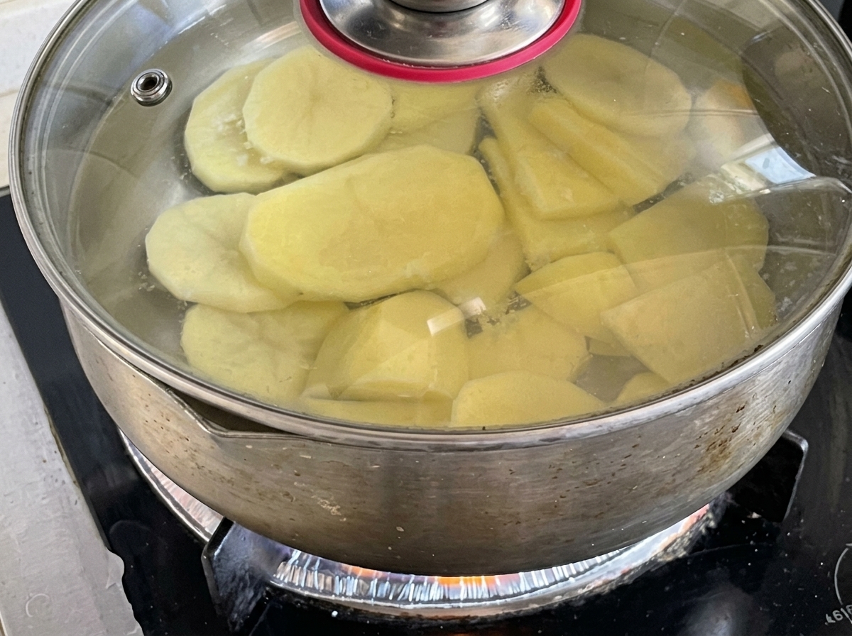 Rodajas de patata hirviendo en una olla tapada sobre la estufa.