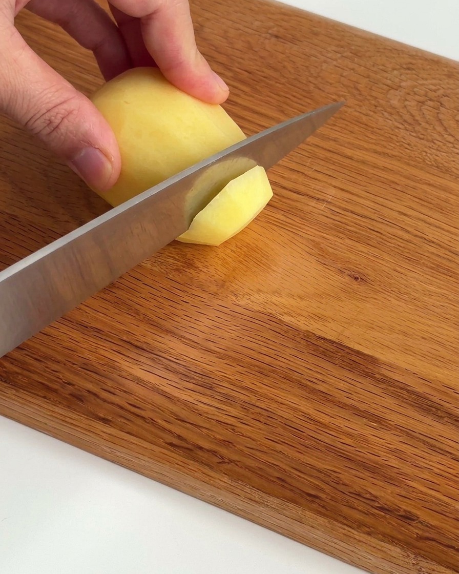 Patatas crudas cortadas en láminas finas y ordenadas sobre una tabla de madera.