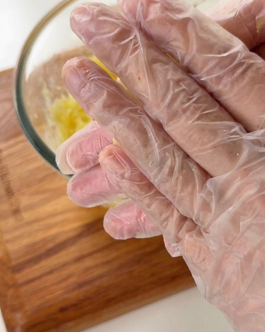 Manos con guantes de plástico dando forma de cuenco a la masa de patata.