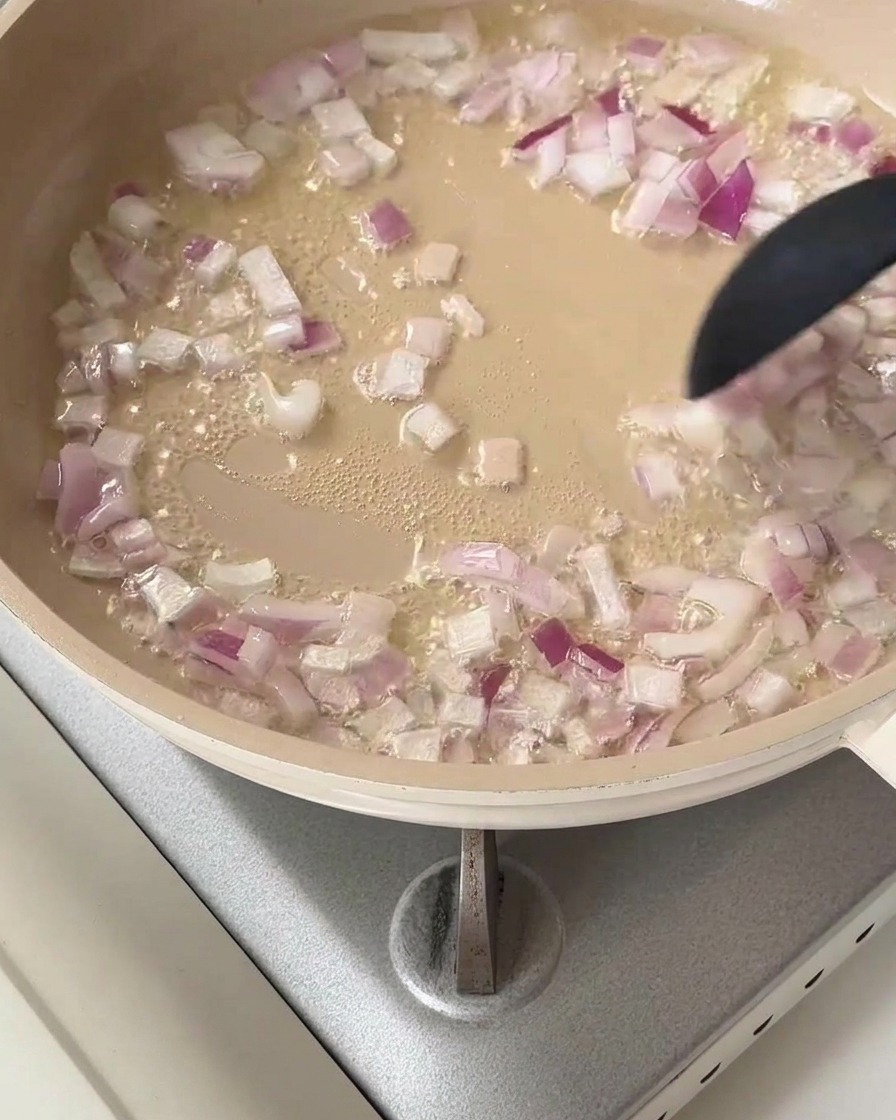 Cebolla roja picada chisporroteando en una sartén con aceite caliente.