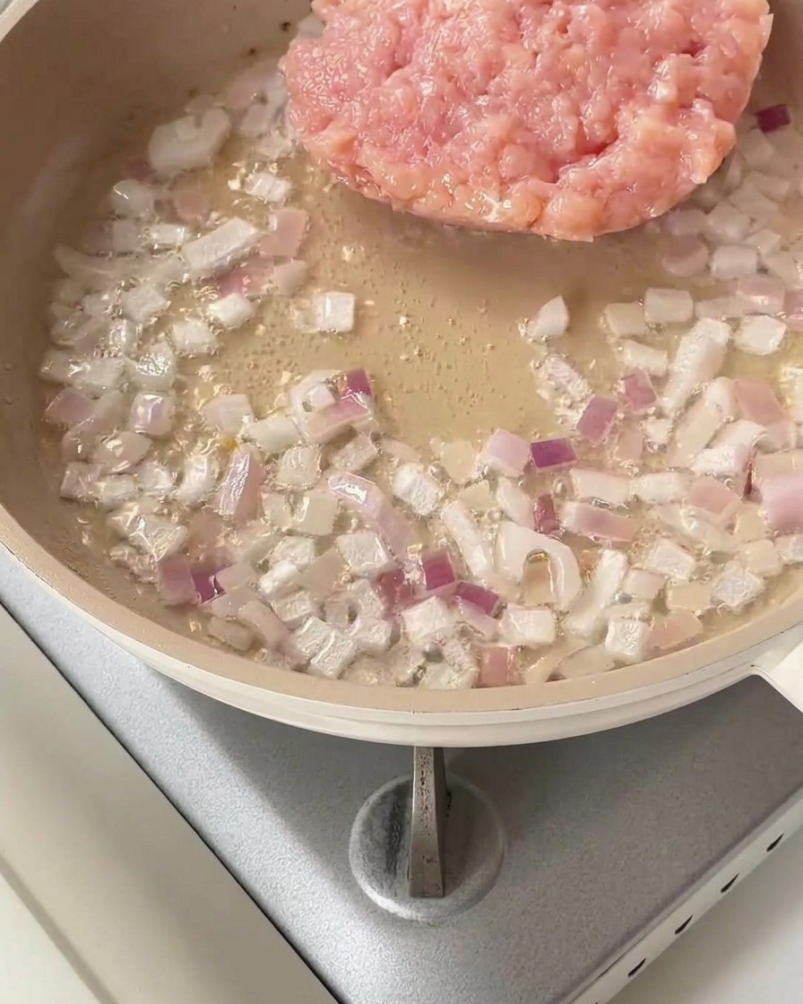 Pollo picado crudo en la sartén junto a la cebolla roja salteada.