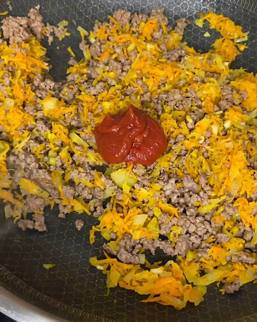 Concentrado de tomate, tomates triturados y salsa de soja siendo mezclados en una preparación de carne dorada, cebolla y zanahoria.