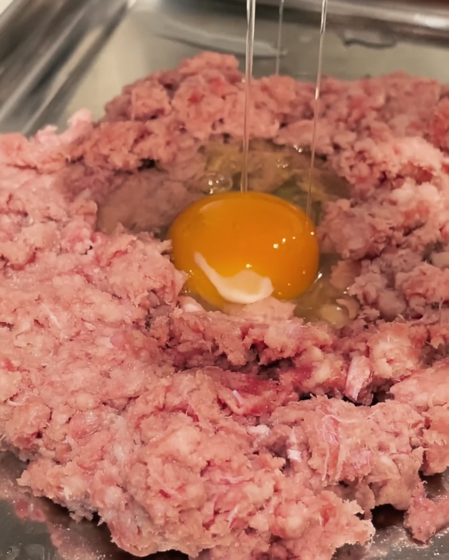 Un huevo crudo cascado en un bol de carne molida.