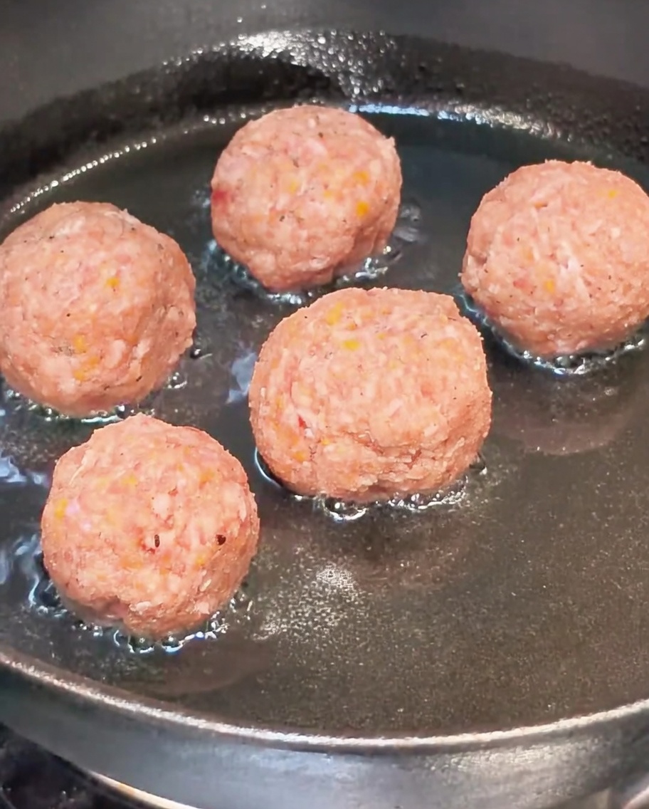 Albóndigas crudas dorándose en una sartén caliente con aceite.