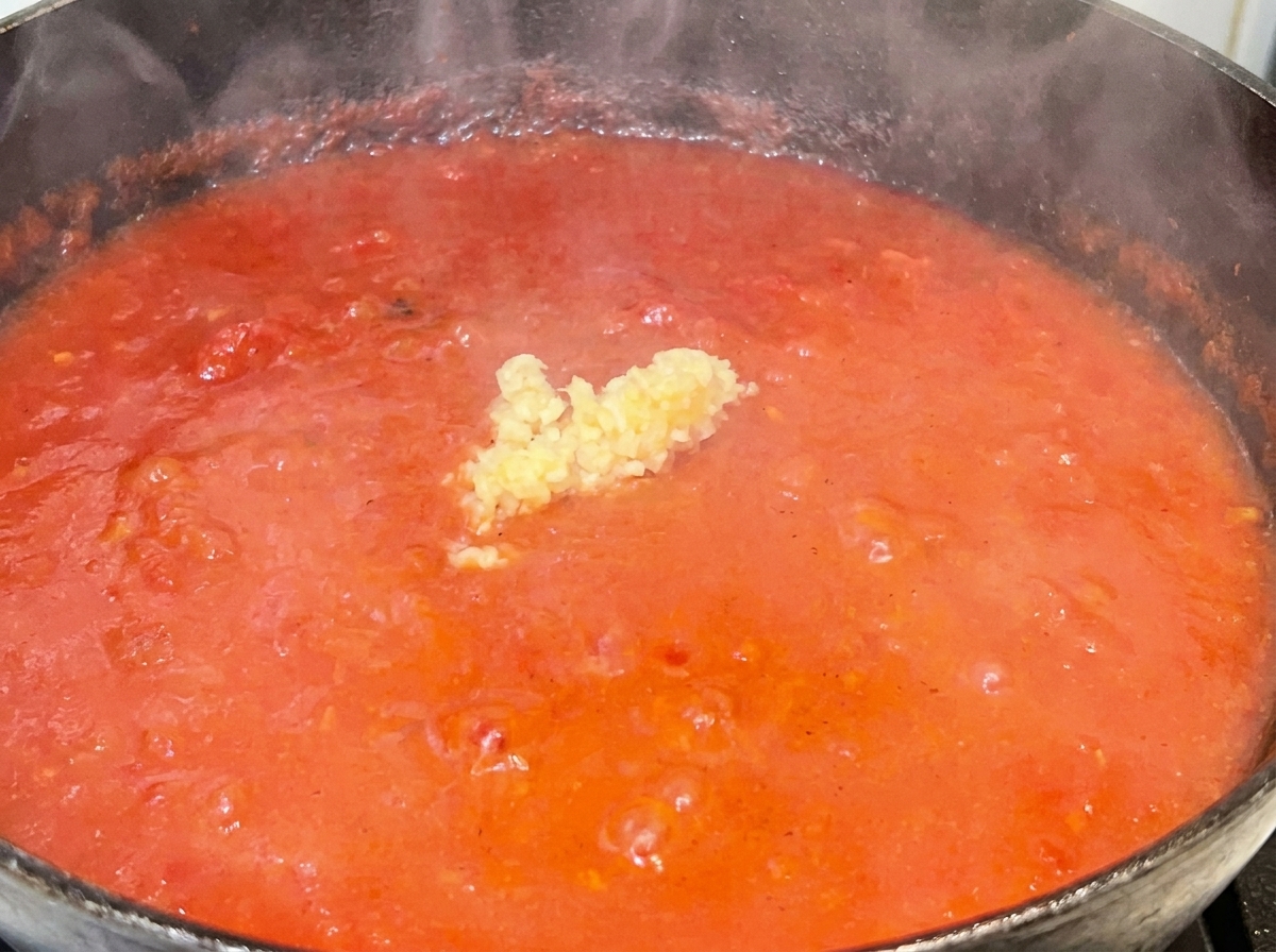 Un pequeño montículo de ajo picado en el medio de una vibrante salsa de tomate roja a fuego lento.