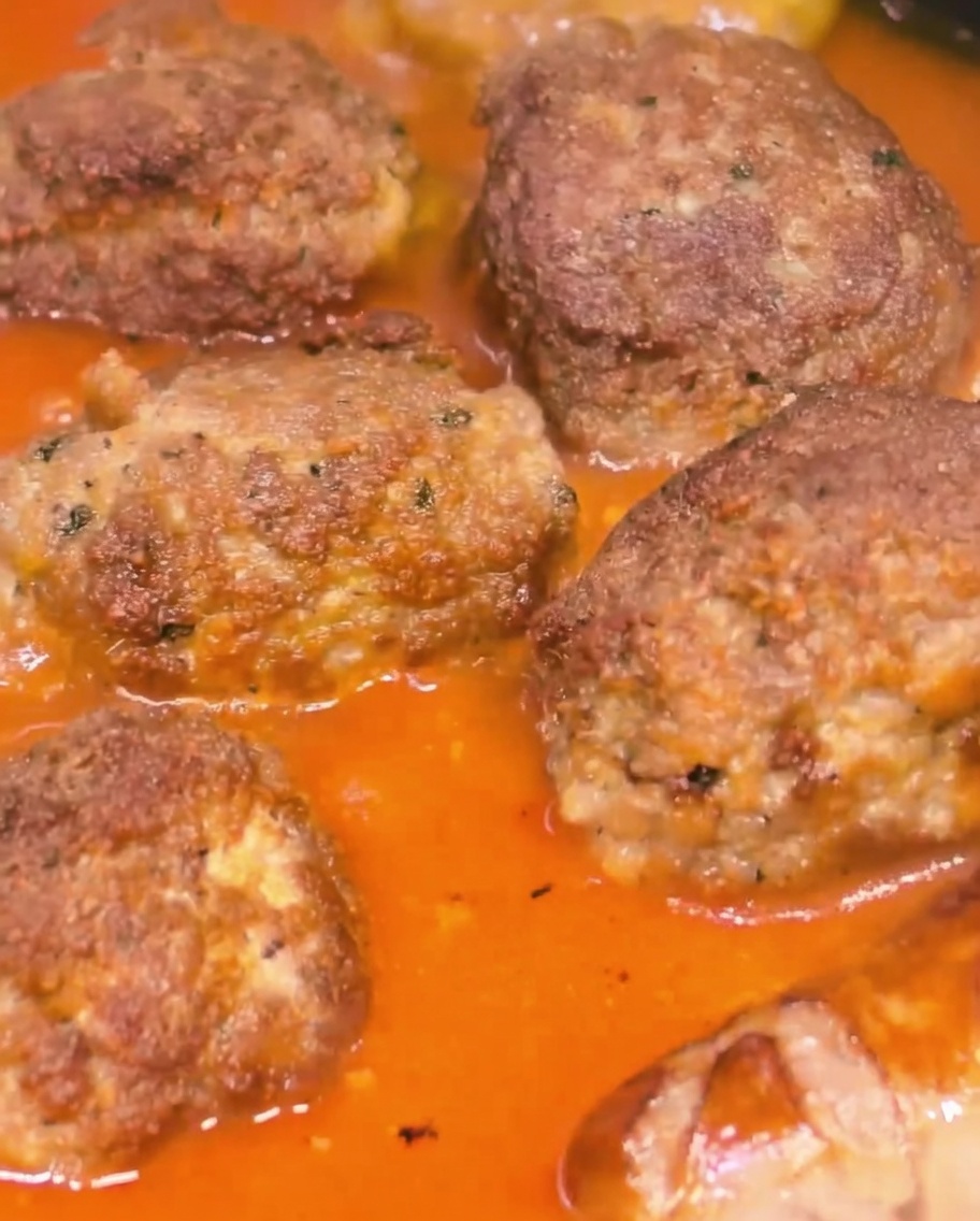 Grandes albóndigas y salchichas cocinándose a fuego lento juntas en una salsa de tomate espesa y rica.