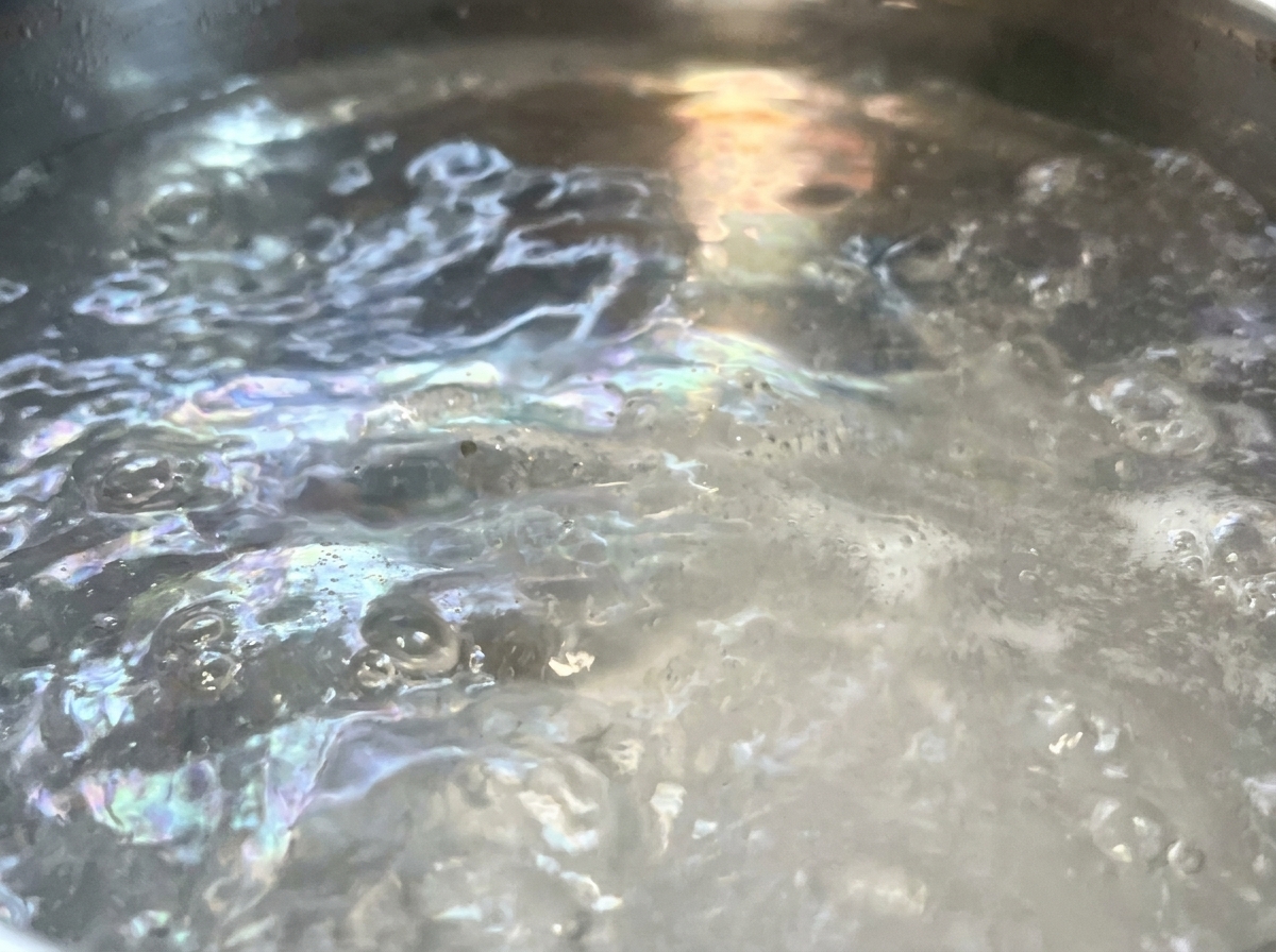 Hilos de espaguetis secos sumergiéndose en una olla grande con agua hirviendo a borbotones.