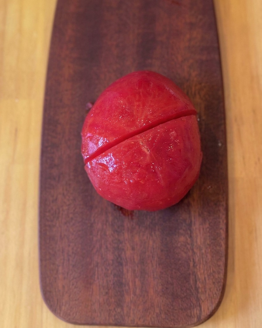 Un tomate asado y pelado sobre una tabla de cortar de madera tras ser cortado por la mitad.