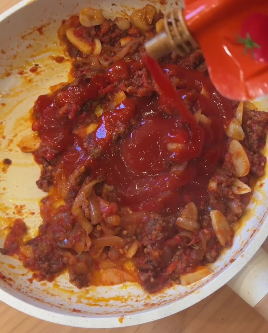 Salsa picante mexicana vertiéndose directamente en la sartén a fuego lento con la carne y los tomates.