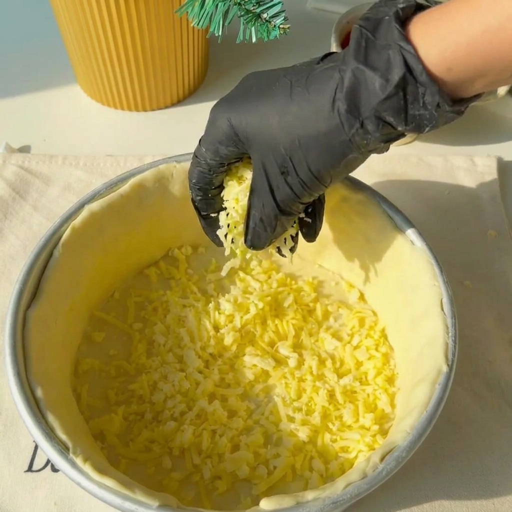 Queso rallado distribuido uniformemente sobre la base de masa.