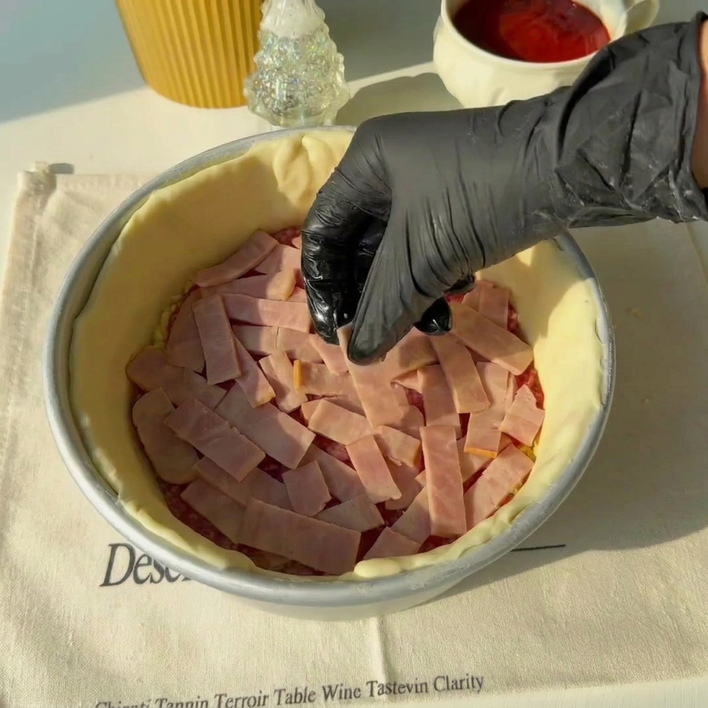 Tiras de jamón siendo distribuidas sobre la capa de salami dentro del molde.