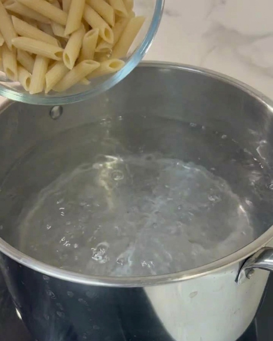Pasta penne siendo añadida a una olla de agua hirviendo.