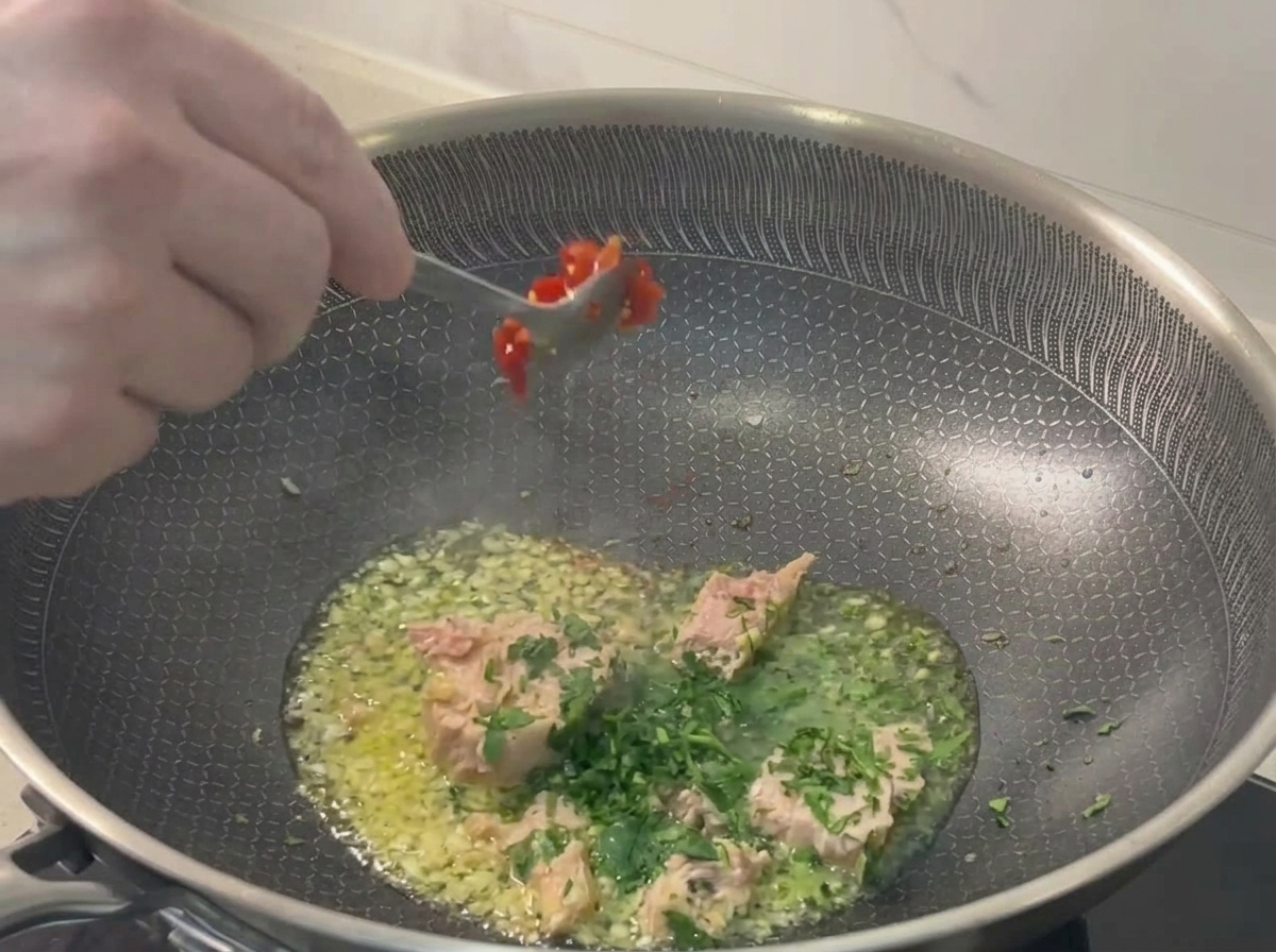 Una cuchara añadiendo chile rojo picado a la sartén.