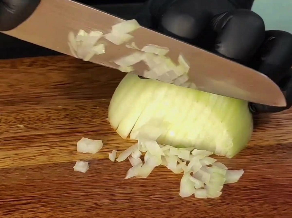 Un cuchillo cortando una cebolla sobre una tabla de cortar de madera.