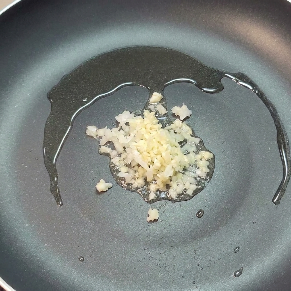 Cebolla y ajo picados sofriéndose en un poco de aceite de oliva en una sartén oscura.