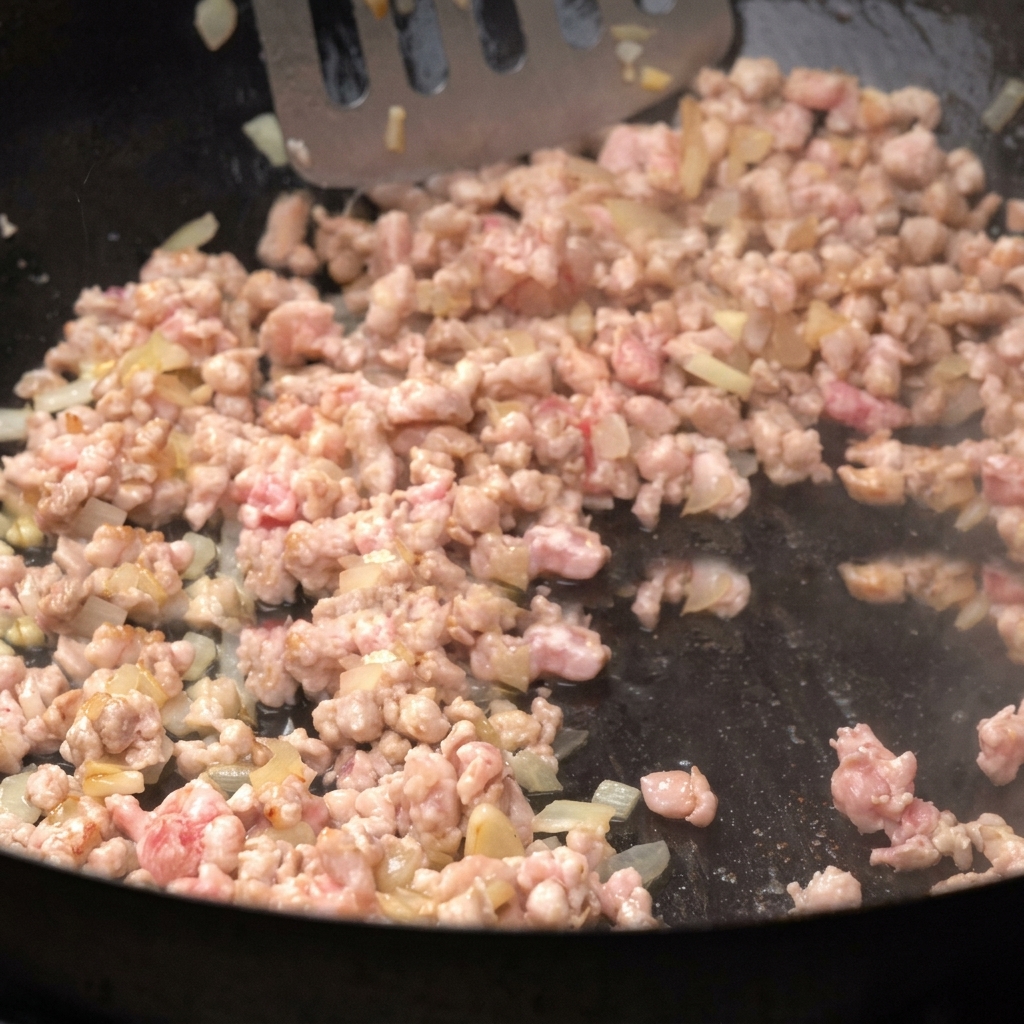 Carne picada dorándose en una sartén junto a cebollas troceadas, siendo removida.