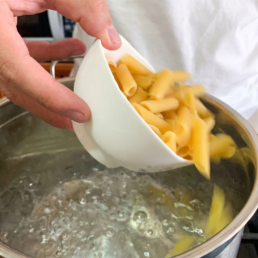 Primer plano de un huevo pochado siendo colocado en el centro de un bol de pasta.