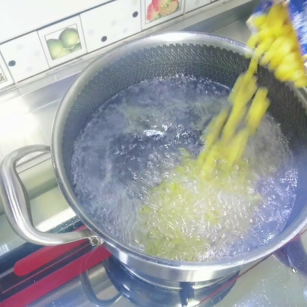 Macarrones amarillos secos vertiéndose desde una bolsa hacia una olla de acero inoxidable con agua hirviendo vigorosamente.