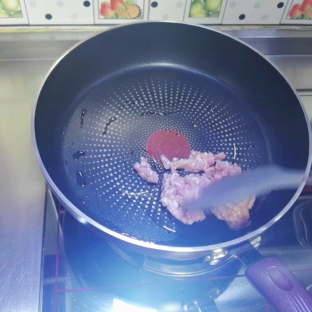 Carne picada cruda siendo salteada en una sartén antiadherente oscura con una espátula de silicona gris.