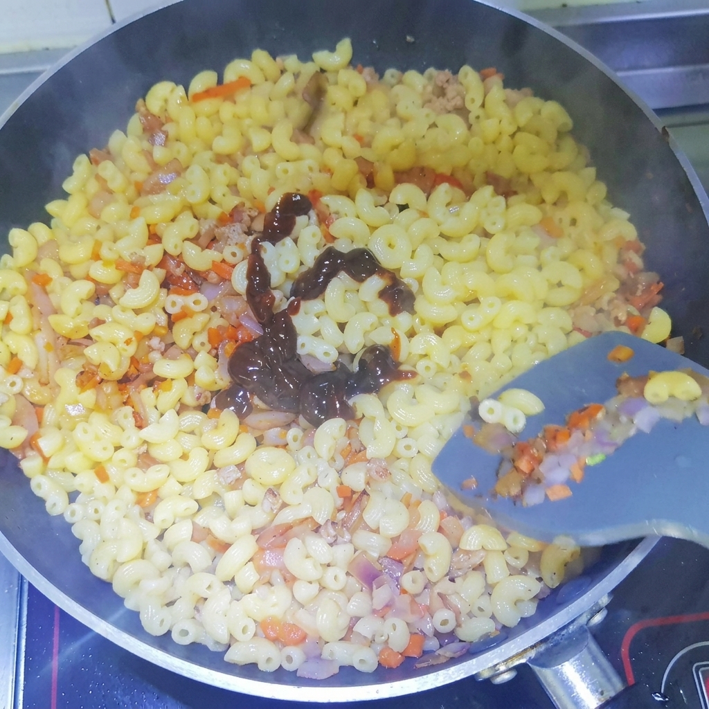 Salsa de pimienta negra oscura siendo exprimida en un patrón de espiral sobre macarrones cocidos en una sartén.