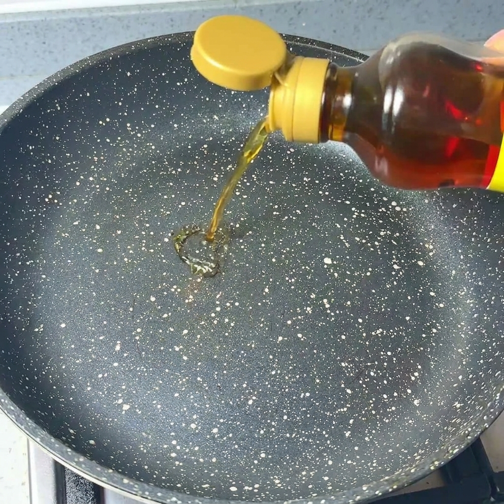 Aceite de sésamo transparente vertiéndose desde una botella a una sartén oscura moteada.