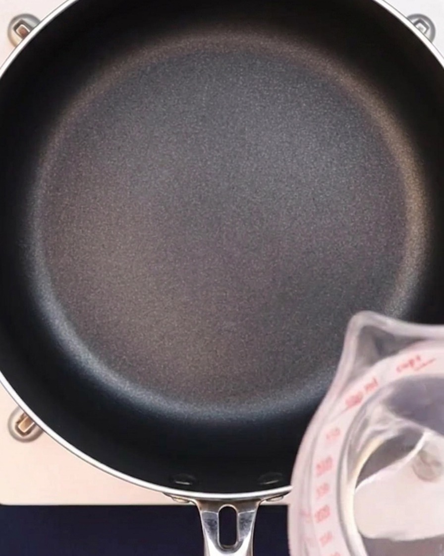 Agua siendo vertida en una sartén negra para iniciar el caldo de curry.
