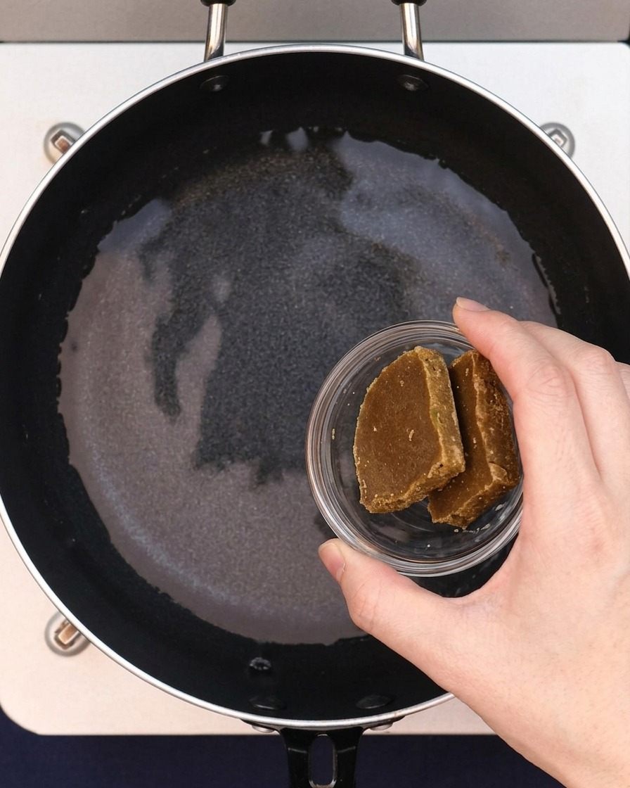 Dos bloques de roux de curry siendo añadidos al agua en la sartén.