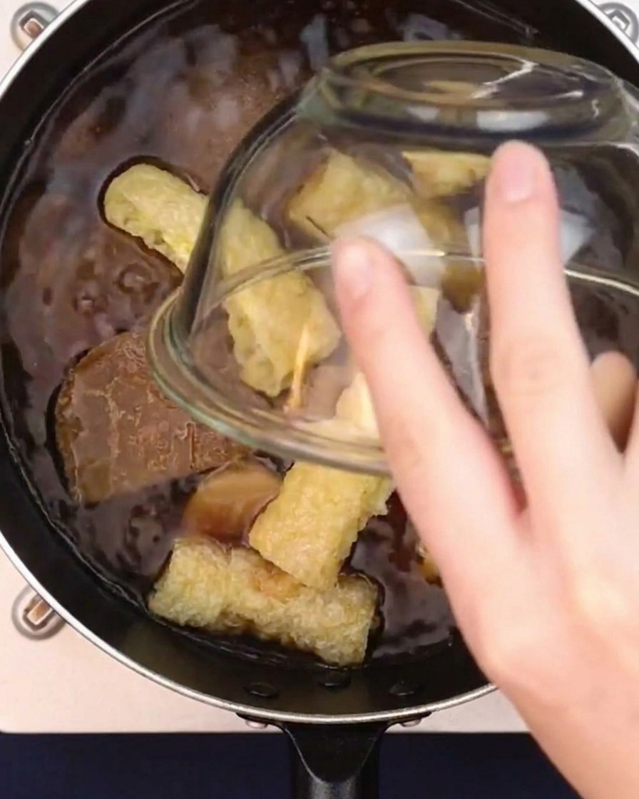 Trocitos de tofu frito inflado cayendo en una olla de caldo de curry japonés a fuego lento.