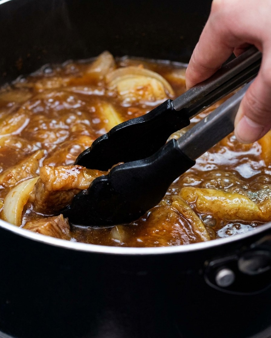 Una olla de caldo de curry con tofu y cebolleta siendo removida con unas pinzas.
