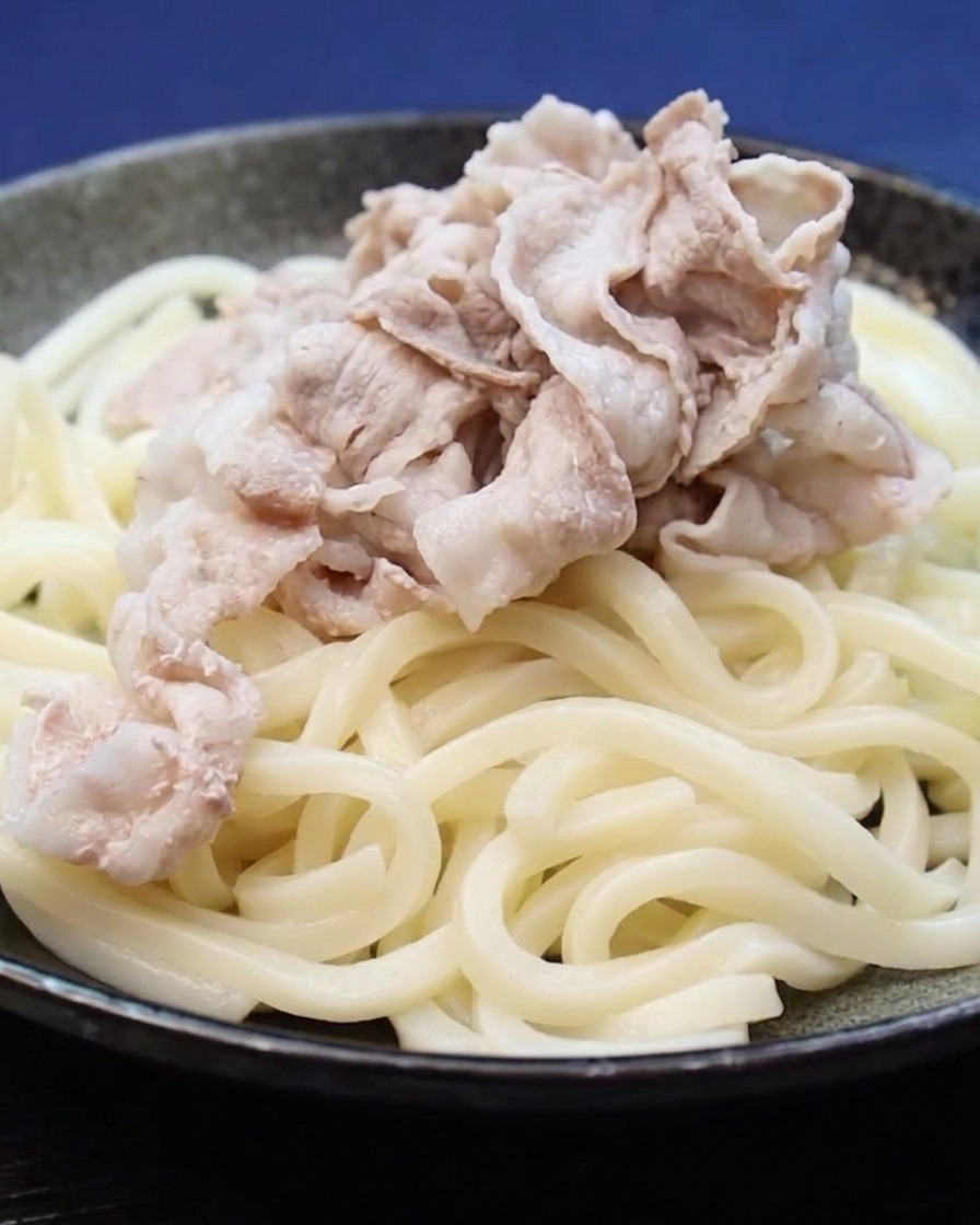 Rodajas de panceta de cerdo cocidas sobre una cama de fideos udon.