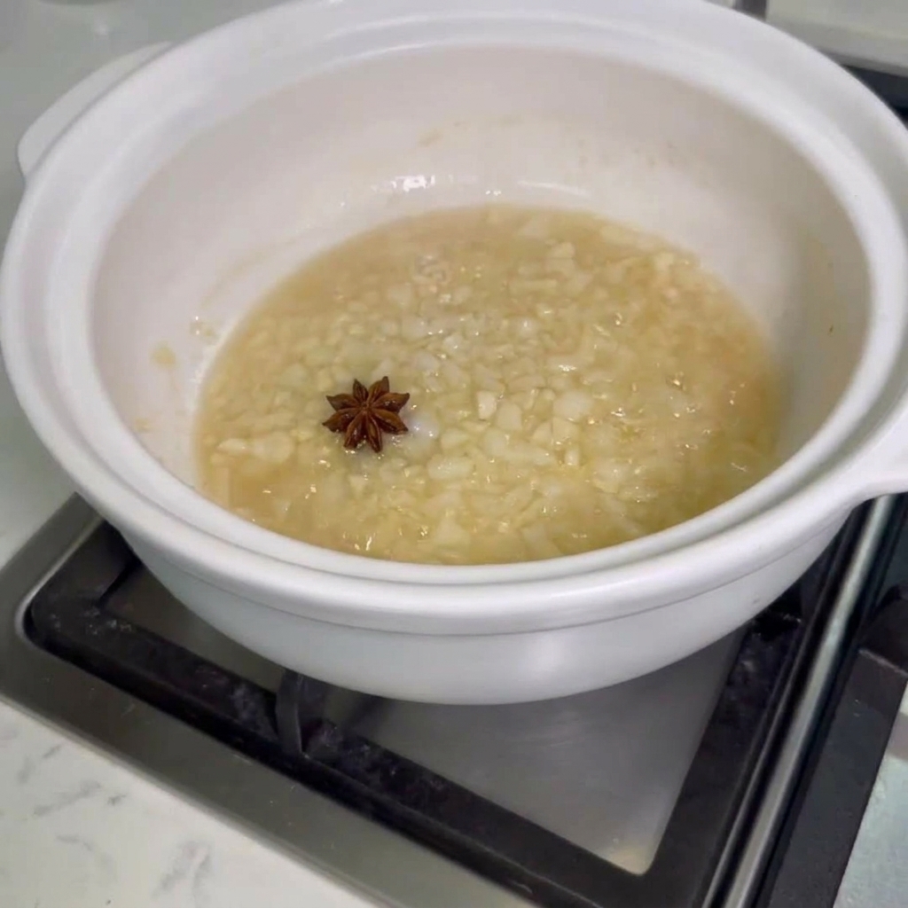 Anís estrellado y alitas de pollo crudas agregándose a la olla con la cebolla y el ajo sofritos.