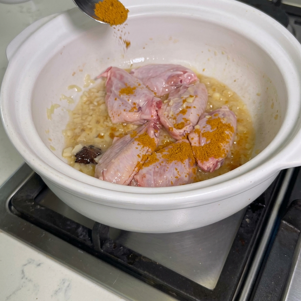 Polvo de curry espolvoreándose sobre las alitas de pollo dentro de la olla.