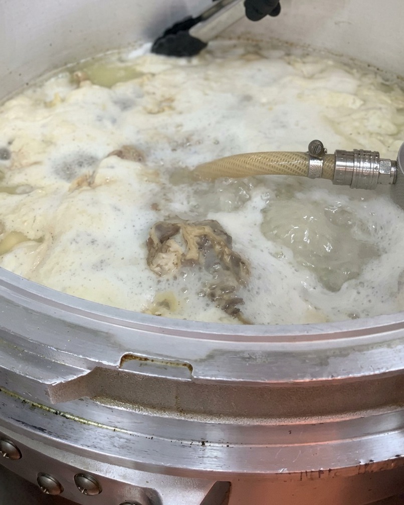 Aceite de pollo siendo vertido en la olla grande de caldo.