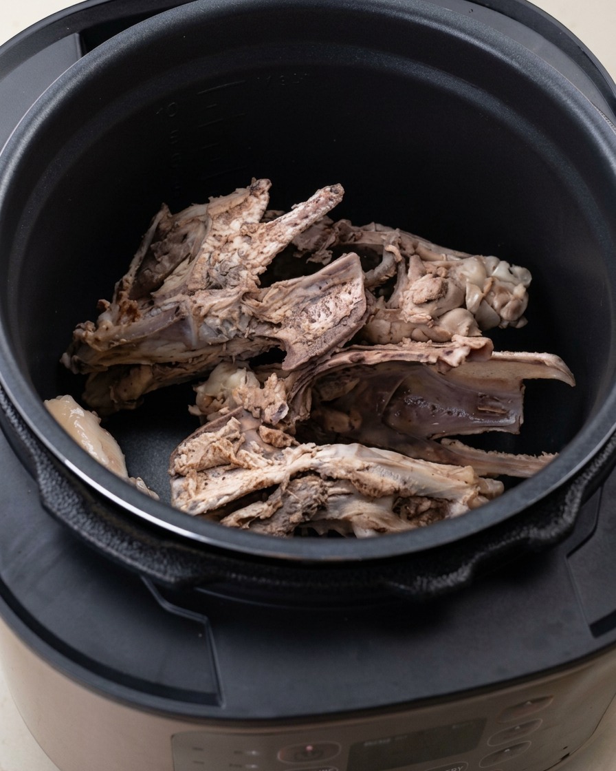 Huesos de pollo y aromáticos como cebolla y jengibre en la olla a presión