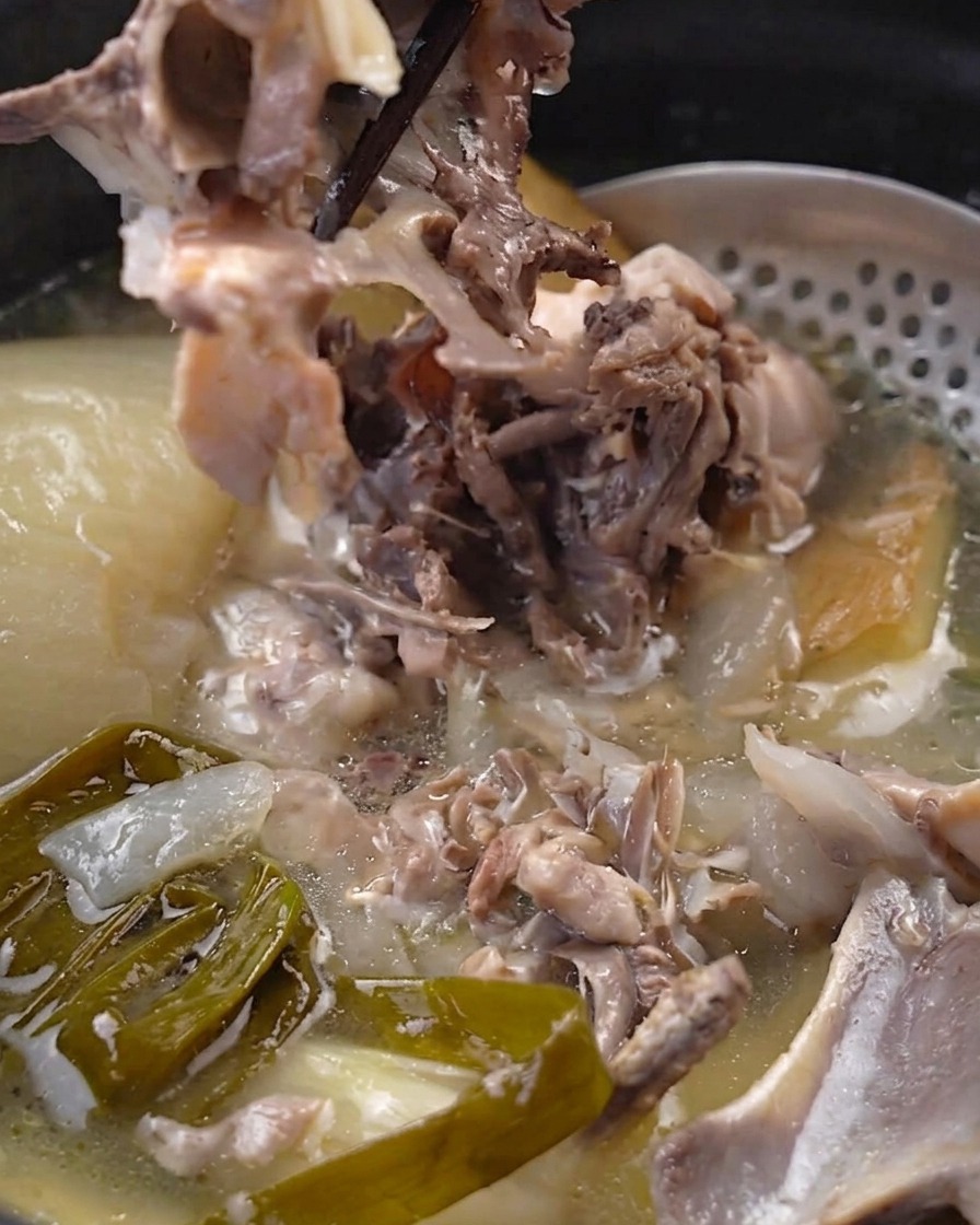 Palillos separando carne de pollo tierna del hueso dentro de la olla