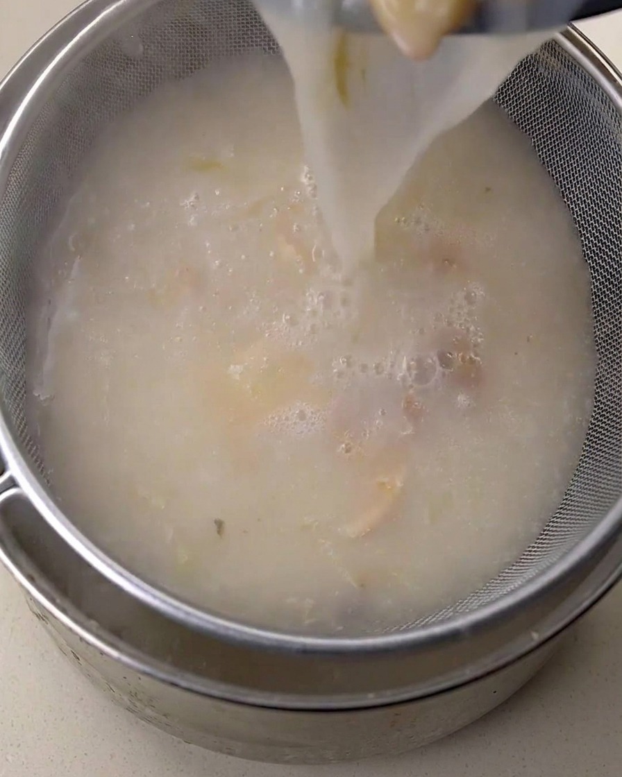 Caldo de pollo blanco cremoso vertido a través de un colador fino en un recipiente