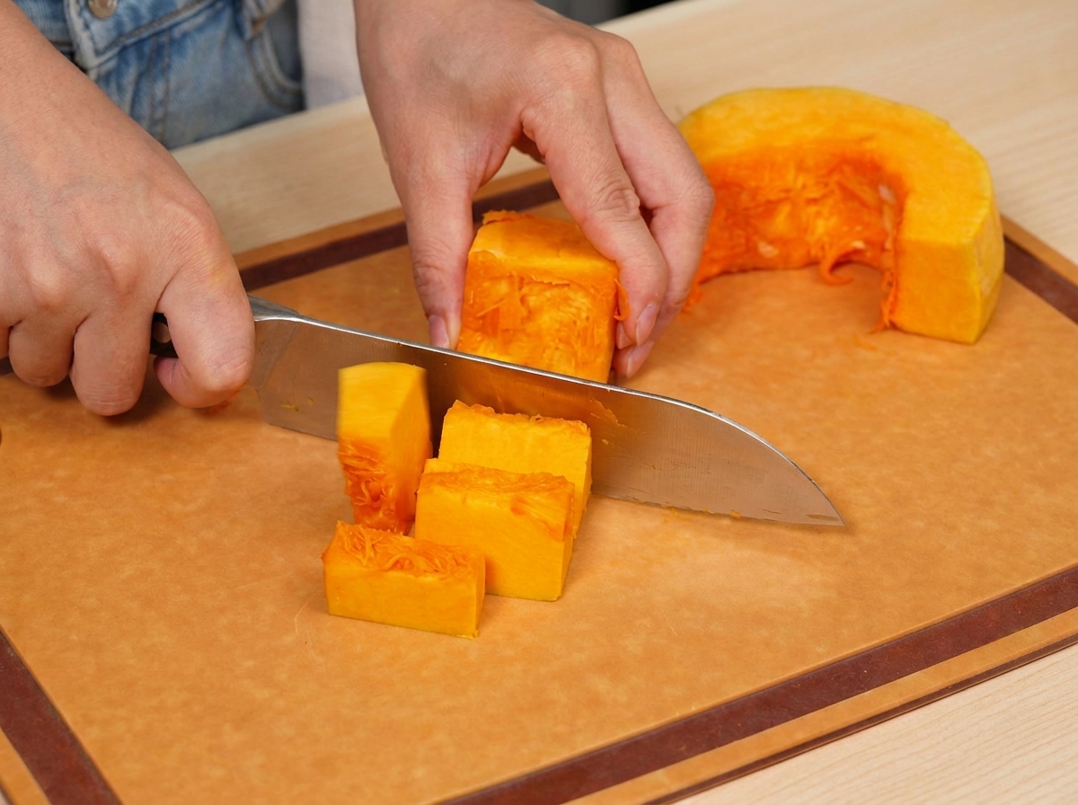 Calabaza naranja fresca siendo cortada cuidadosamente en cubos pequeños y uniformes sobre una tabla de madera.