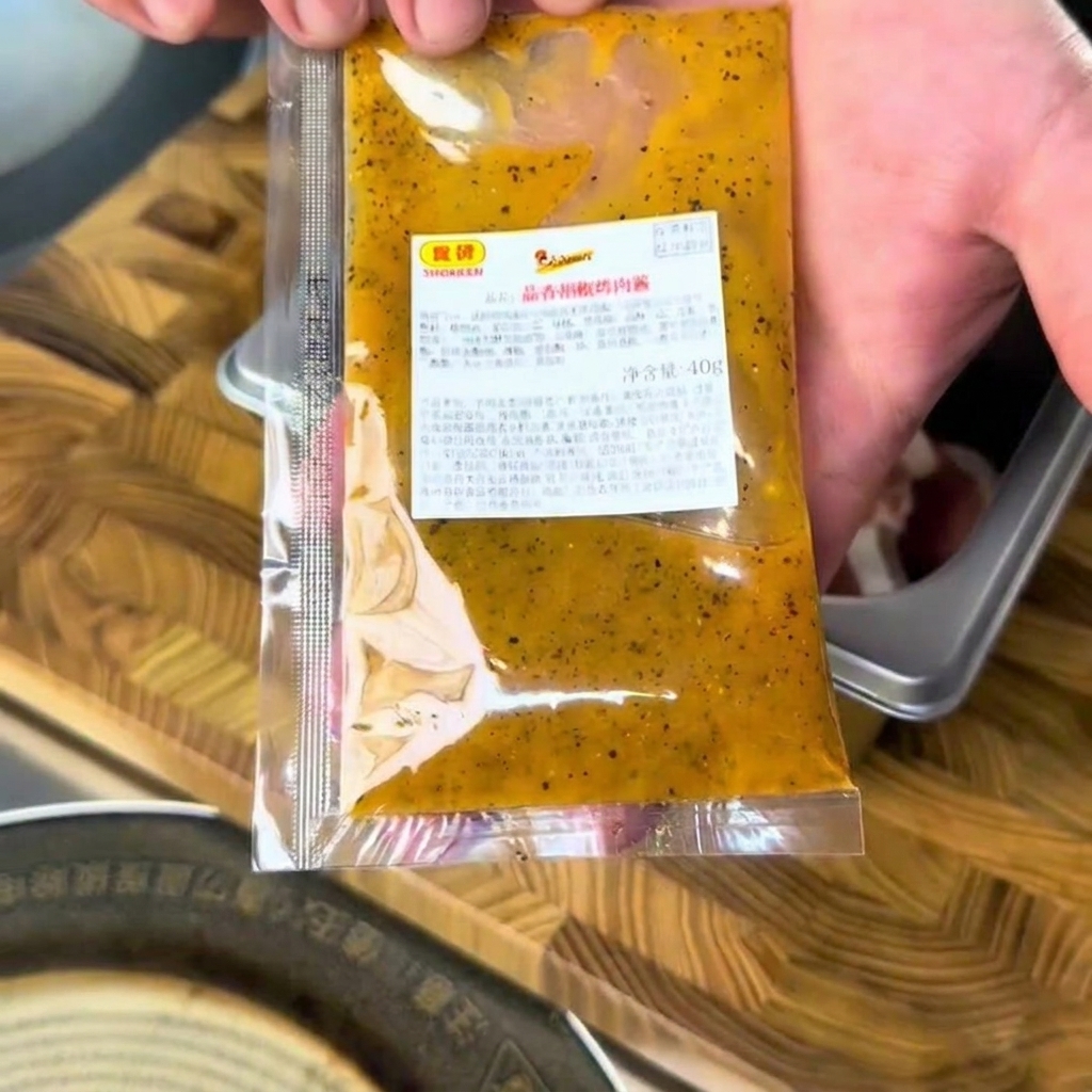 Un paquete de salsa barbacoa de ajo y pimienta exprimiéndose sobre filetes de ternera crudos en un recipiente de metal.
