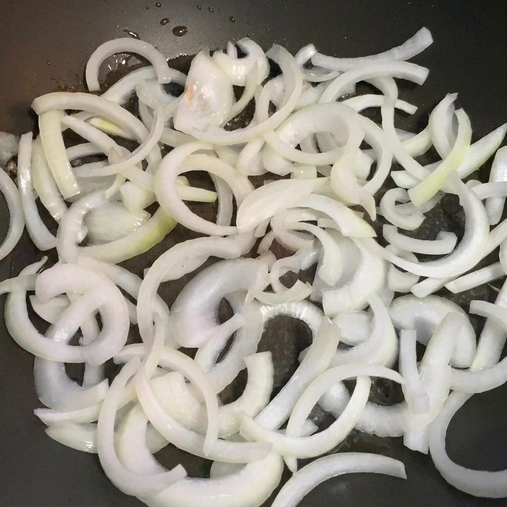 Rodajas de cebolla cocinándose en una sartén hasta quedar transparentes.