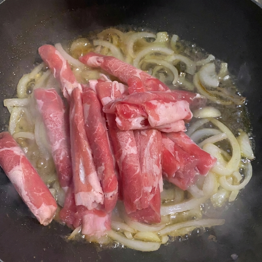 Láminas de ternera añadidas a la sartén con cebolla y agua.