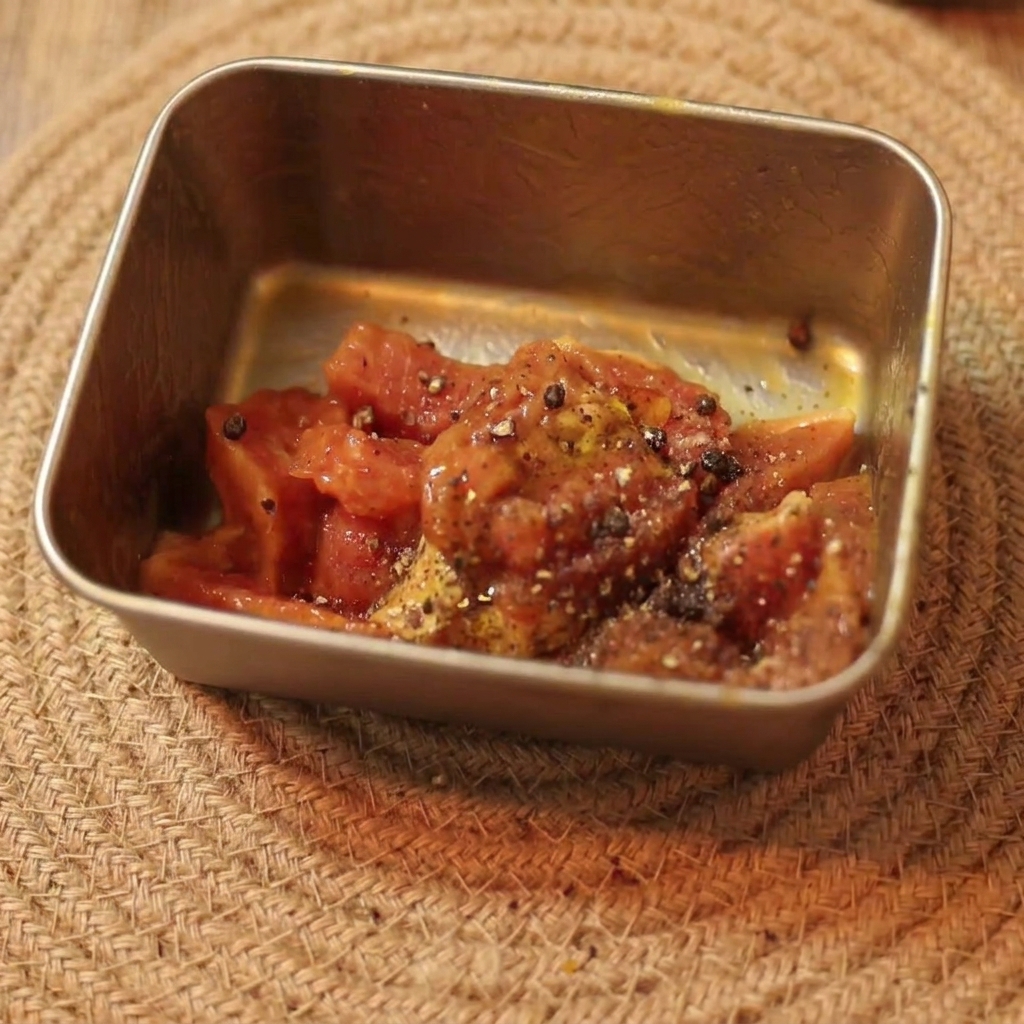 Ternera cruda en tiras marinada sazonada con pimienta negra y aceite en un pequeño recipiente rectangular.