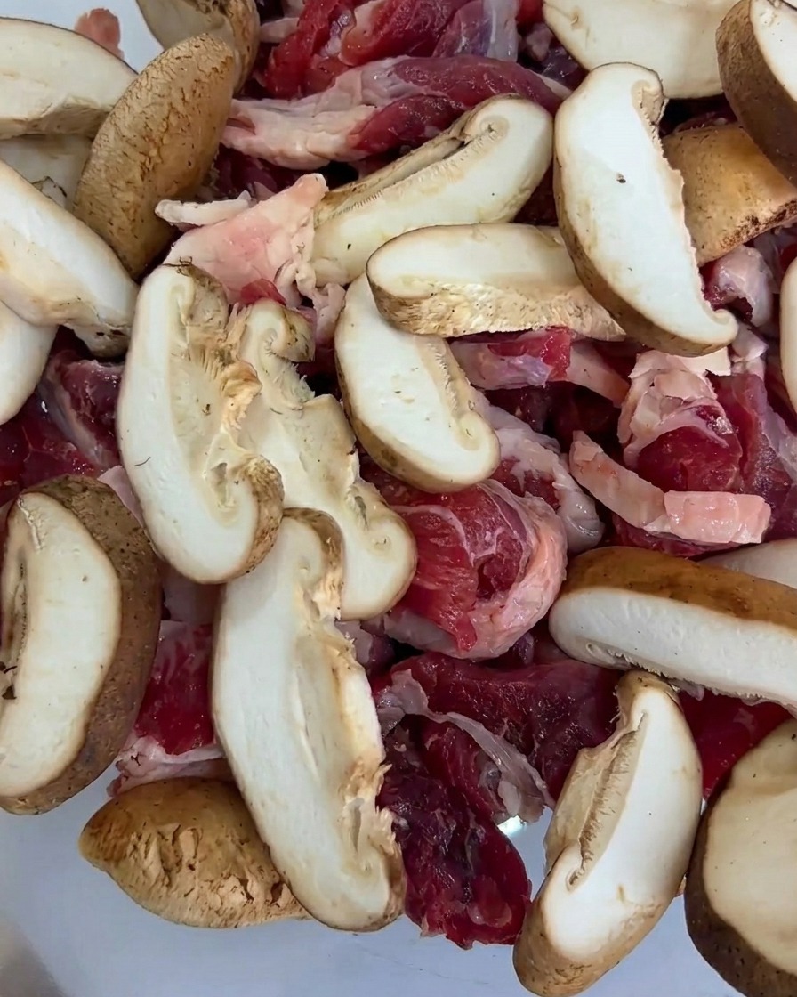 Trozos frescos de maíz baby añadidos a la bandeja, mezclados con la ternera y las rodajas de champiñón.