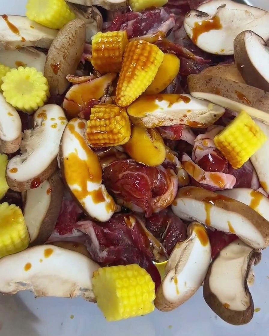 Salsa de soja de mariscos y salsa de ostras vertiéndose sobre la mezcla de ternera cruda, champiñones y maíz baby.