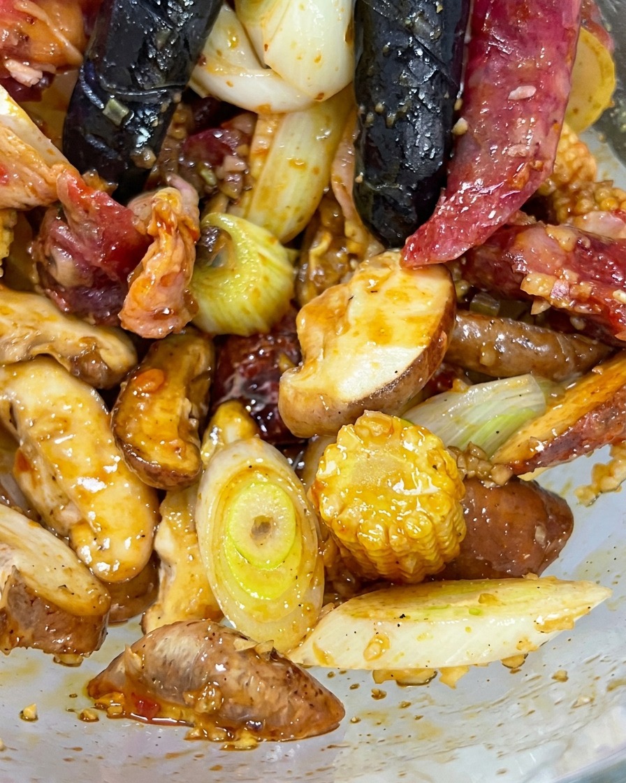 Manos con guantes mezclando la ternera, los champiñones, el maíz baby y los aromáticos en un bol de cristal.