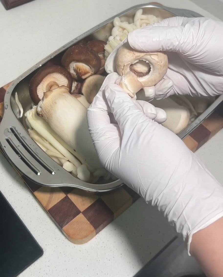 Una mano quitando el tallo de un sombrero de seta shiitake cruda y entera.